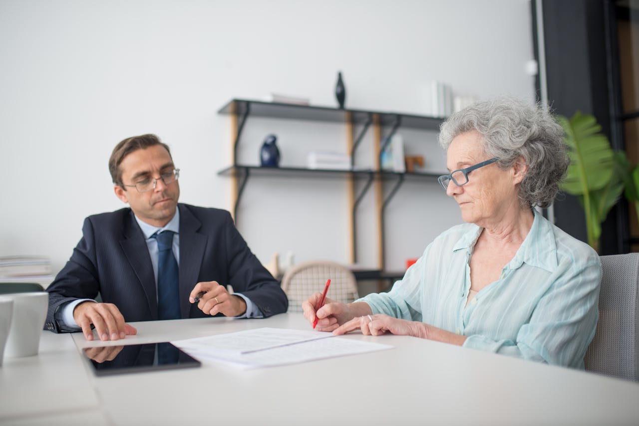 Elderly woman signing paperwork in modern office with consultant.